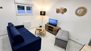 A living room with a blue sofa, a grey ottoman, a wooden TV stand, and a floor lamp.