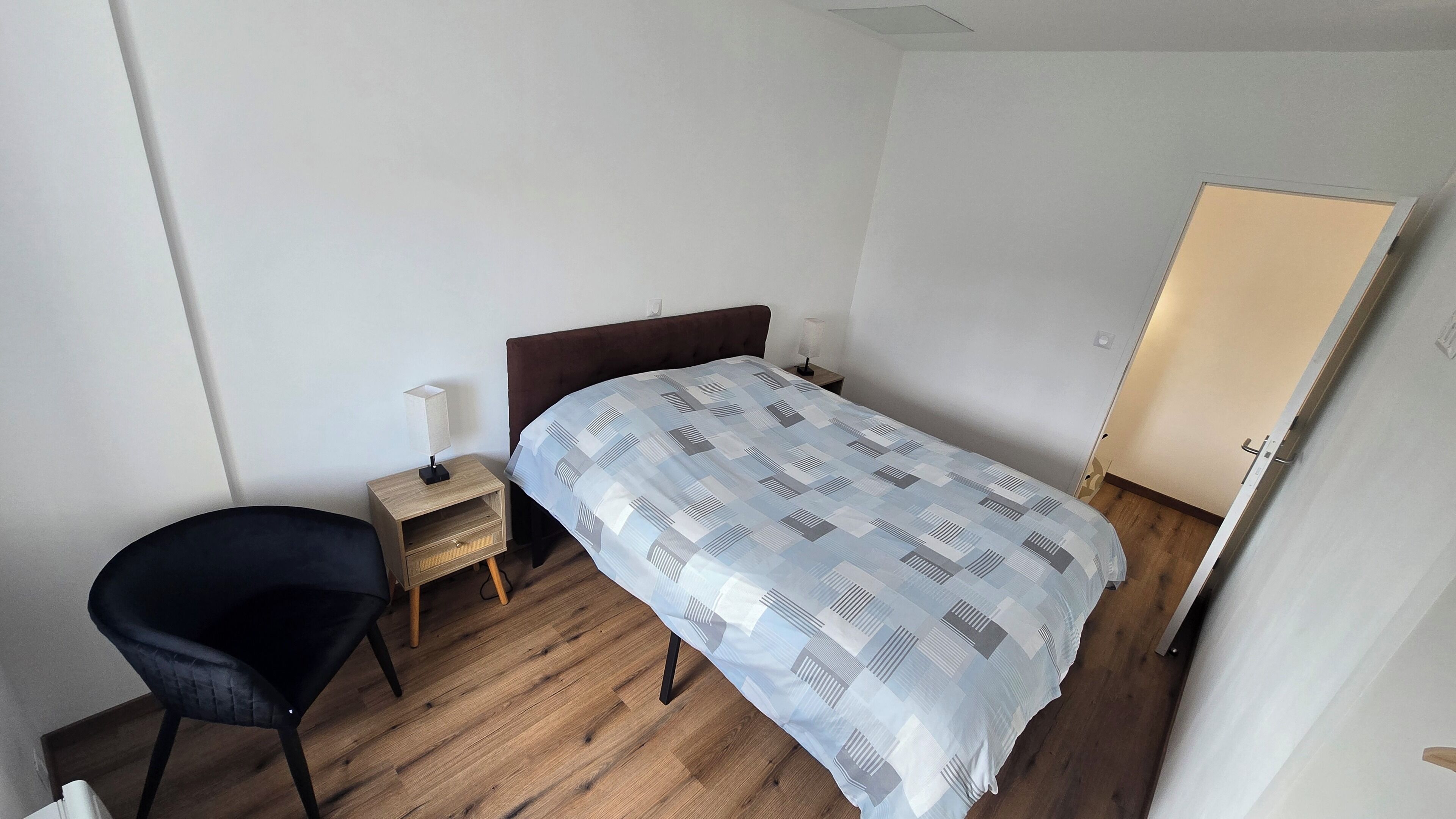 Une petite chambre à coucher, bien rangée, avec un lit simple, une table de chevet avec une lampe, une chaise et une armoire.
