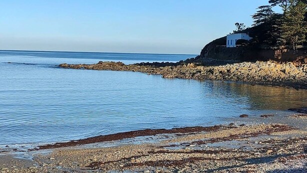 A coastal scene with a rocky shoreline, calm water, and a building on a cliff.