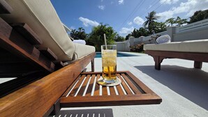 Un'area piscina con una sedia a sdraio in legno e un bicchiere di bevanda fresca su un sottobicchiere.