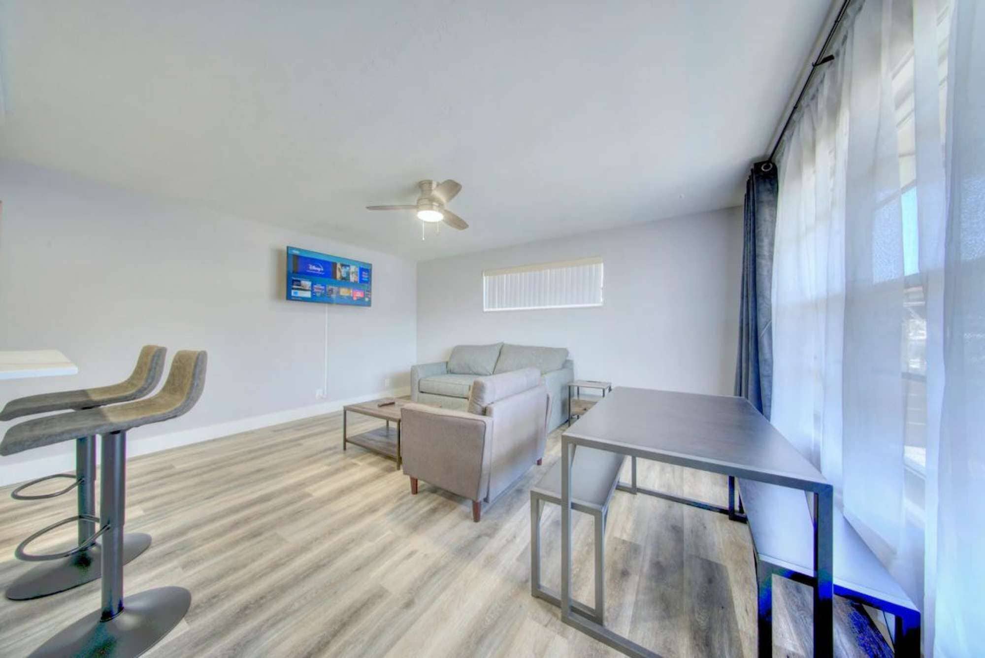 A modern living room with a grey sofa, a coffee table, a TV mounted on the wall, and a ceiling fan.