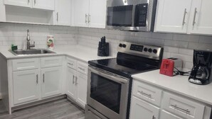 A modern kitchen with white cabinets, stainless steel appliances, and a tiled backsplash. - Mahalo Waterfront 1 BR Apartment (Fort Lauderdale)