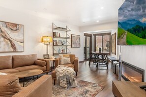 A living room with a sofa, coffee table, and a rug. There is a dining area with a table and chairs.
