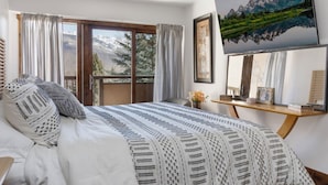 Une chambre à coucher avec un lit, une table de chevet en bois, un tableau et une vue sur les montagnes par la fenêtre.