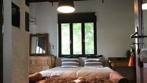 Et soveværelse med en stor seng, et vindue med udsigt over grøn vegetation, en kommode og et spejl.
