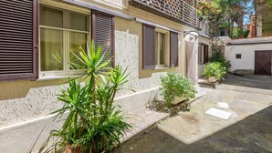 A building with multiple windows and shutters, a small garden area with potted plants, and a paved courtyard. - Vacation home Elena by Interhome (Castiglione della Pescaia)