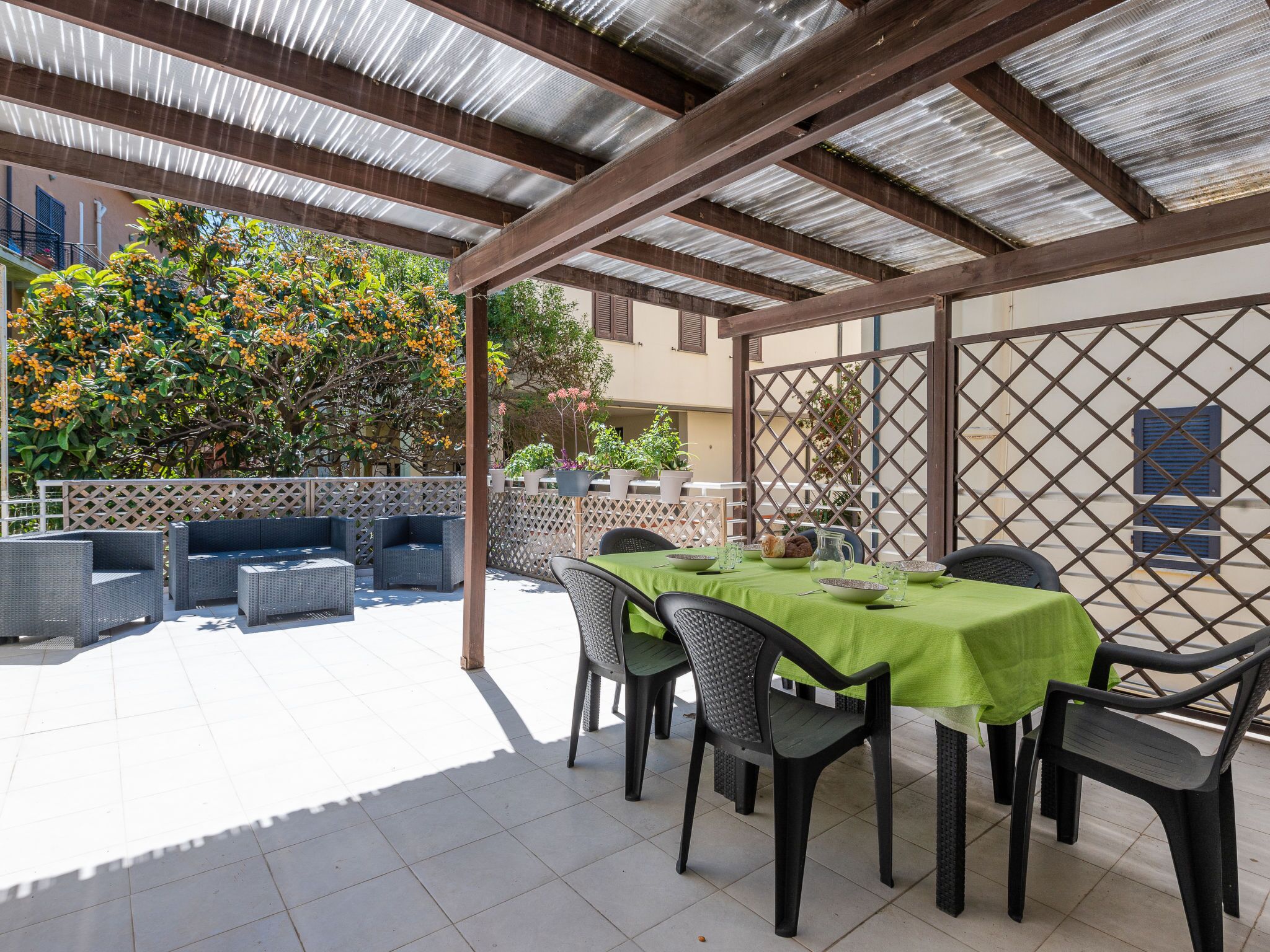 An outdoor patio with a covered seating area, a table set for dining, and potted plants.