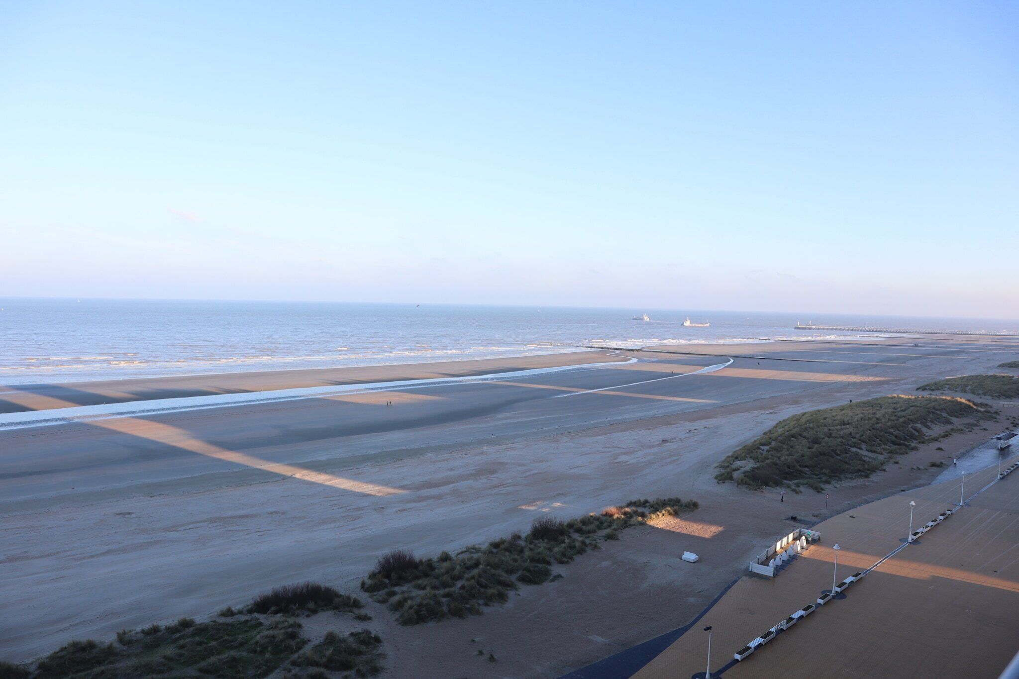 A coastal landscape with a sandy beach, a road curving through the area, and a distant ship.