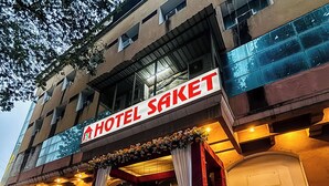 A hotel entrance with a sign reading "HOTEL SAKET," a red awning, and potted plants. - Hotel Saket (Prayagraj)