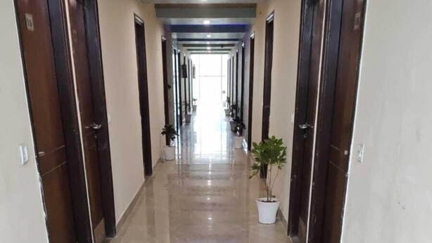A corridor with marble flooring, wooden doors, and potted plants. - Hotel Saket (Prayagraj)