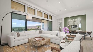 A spacious living room with a large white sectional sofa, a wooden coffee table, and a view of the ocean through large windows. - Amaui Villas 11 Three Bedroom (Kamuela)