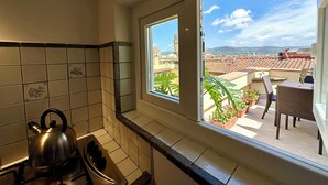 A kitchen with a view of a cityscape through a window, a kettle on the stove, and a balcony with plants. - Florence Rooftop Apt - Jacuzzi & Panoramic View (Firenze)
