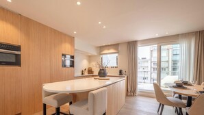 A modern kitchen with wooden cabinets, a central island with seating, built-in ovens, and a large window with curtains.