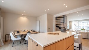 Una cocina moderna con una isla central, comedor con sillas y una escalera que sube a otro nivel.