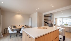A modern kitchen with a central island, dining area with chairs, and a staircase leading to another level.