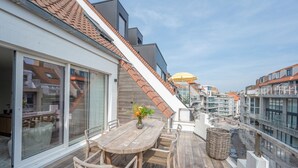 Una terraza de madera con una mesa y sillas, una cesta de mimbre y un cartel que indica 'Floor 1 Seaside'.