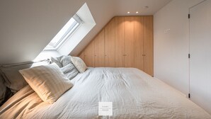 A bedroom with a sloped ceiling, a skylight, a bed with pillows, and wooden wardrobes.