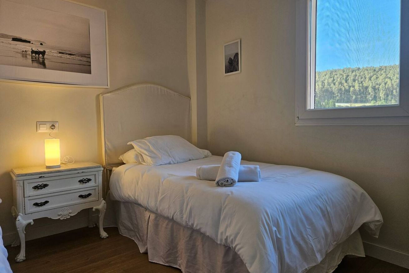 Un lit bien fait, avec du linge de lit blanc, une lampe de chevet et un tableau encadré au mur.
