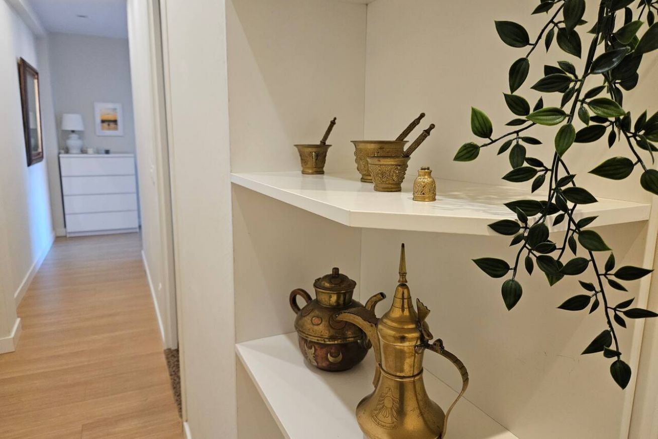 Pasillo con un estante blanco que muestra utensilios de cocina de latón y una planta.