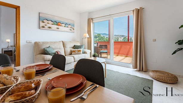 A dining area with a table set for two, a sofa, and a painting above the sofa. - Amazing Sea and Golf Course view 2BR, Parking Pool REF037 (Benalmádena)