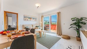 A modern hotel room with a balcony, a dining area with breakfast, and a large potted plant. - Amazing Sea and Golf Course view 2BR, Parking Pool REF037 (Benalmádena)