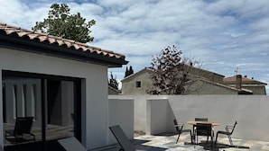A patio with lounge chairs and a table, a building with a tiled roof, and a clear sky. - Maison Magnifique Carcassonne (Carcassonne)