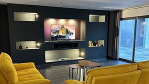 A modern living room with a large flat-screen TV, two yellow sofas, and a large window offering a view of the sea. - Maison Magnifique Carcassonne (Carcassonne)