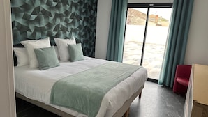 A modern bedroom with a geometric-patterned headboard, a large bed with multiple pillows, and a view of the outdoors through a sliding door. - Maison Magnifique Carcassonne (Carcassonne)