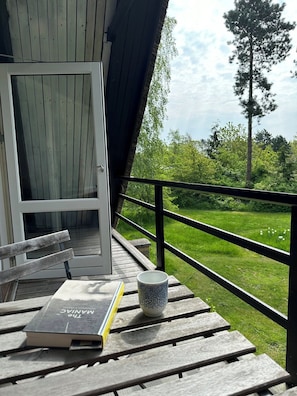 Une terrasse en bois avec un banc, un livre intitulé « Le Manuel » et une tasse.