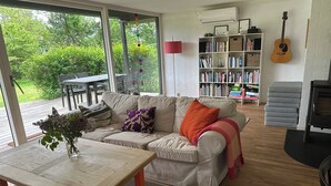 A living room with a sofa, a wooden table, a bookshelf, and a guitar. - Cozy, thatched cottage with modern décor (Knebel)