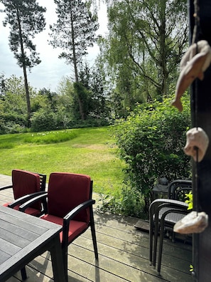 A deck with a table and chairs, surrounded by greenery and trees.