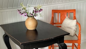 A dark wooden table with a vase of flowers, an orange chair with a cushion, and a white paneled wall. - Cozy, thatched cottage with modern décor (Knebel)
