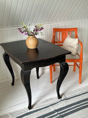 A dark wooden table with a vase of flowers, an orange chair with a cushion, and a white paneled wall.