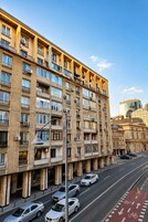 Un edificio de varios pisos con balcones, una calle con coches y un carril bici.