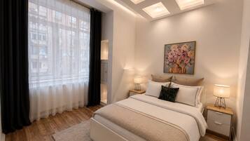 Un dormitorio con cama, lámparas de noche, un cuadro y una ventana con cortinas.
