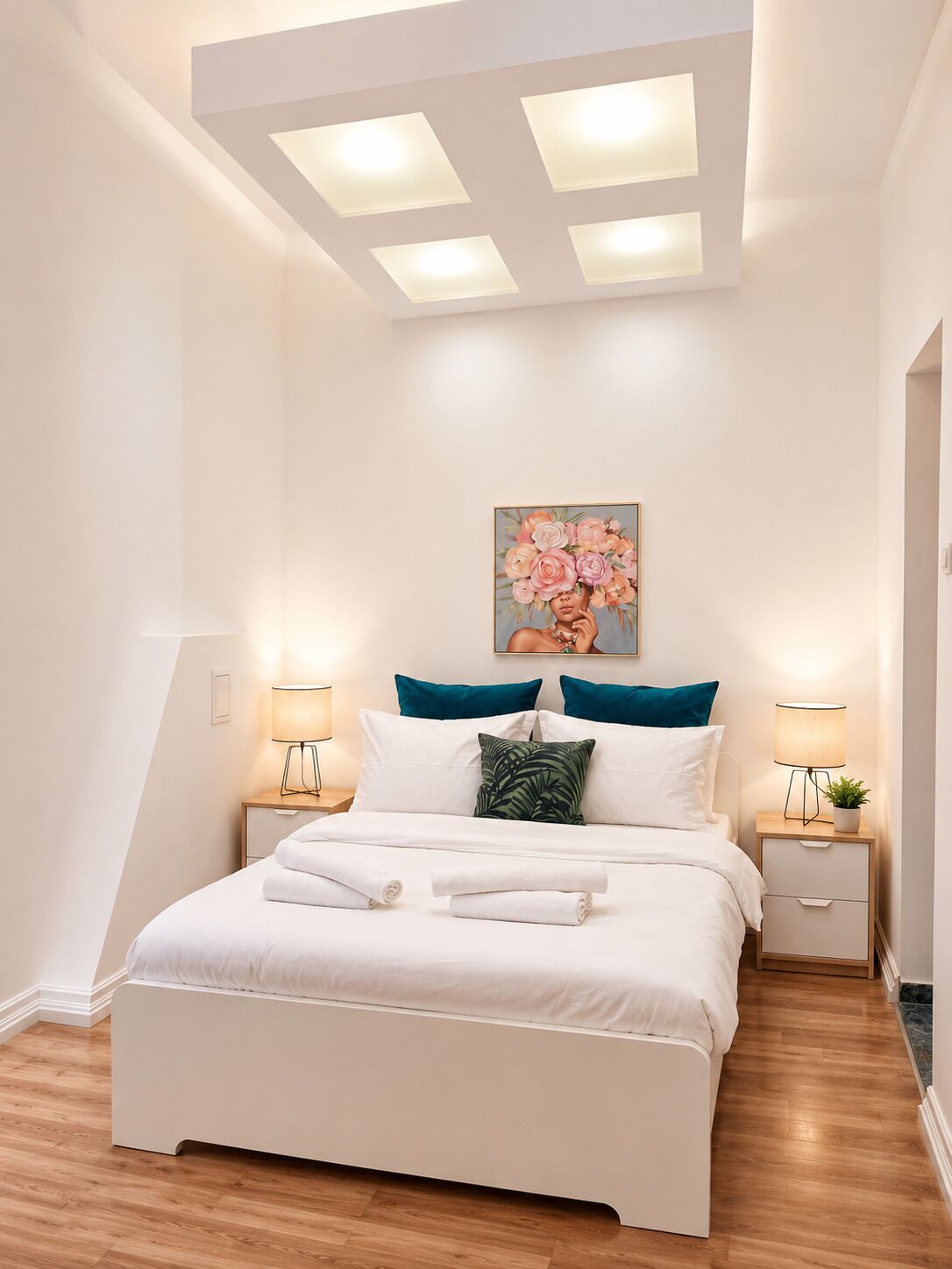 Un dormitorio con cama, dos mesitas de noche, una lámpara en el techo y un cuadro colgado en la pared.