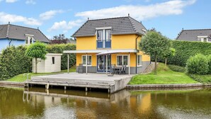 Ein gelbes Haus mit einem Steg, der in ruhiges Wasser ragt, umgeben von viel Grün.