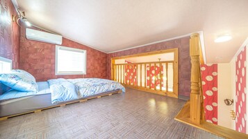 Un dormitorio con piso de madera, una cama con cubrecama floral, una ventana con persianas y una baranda de madera con diseño rojo y blanco.