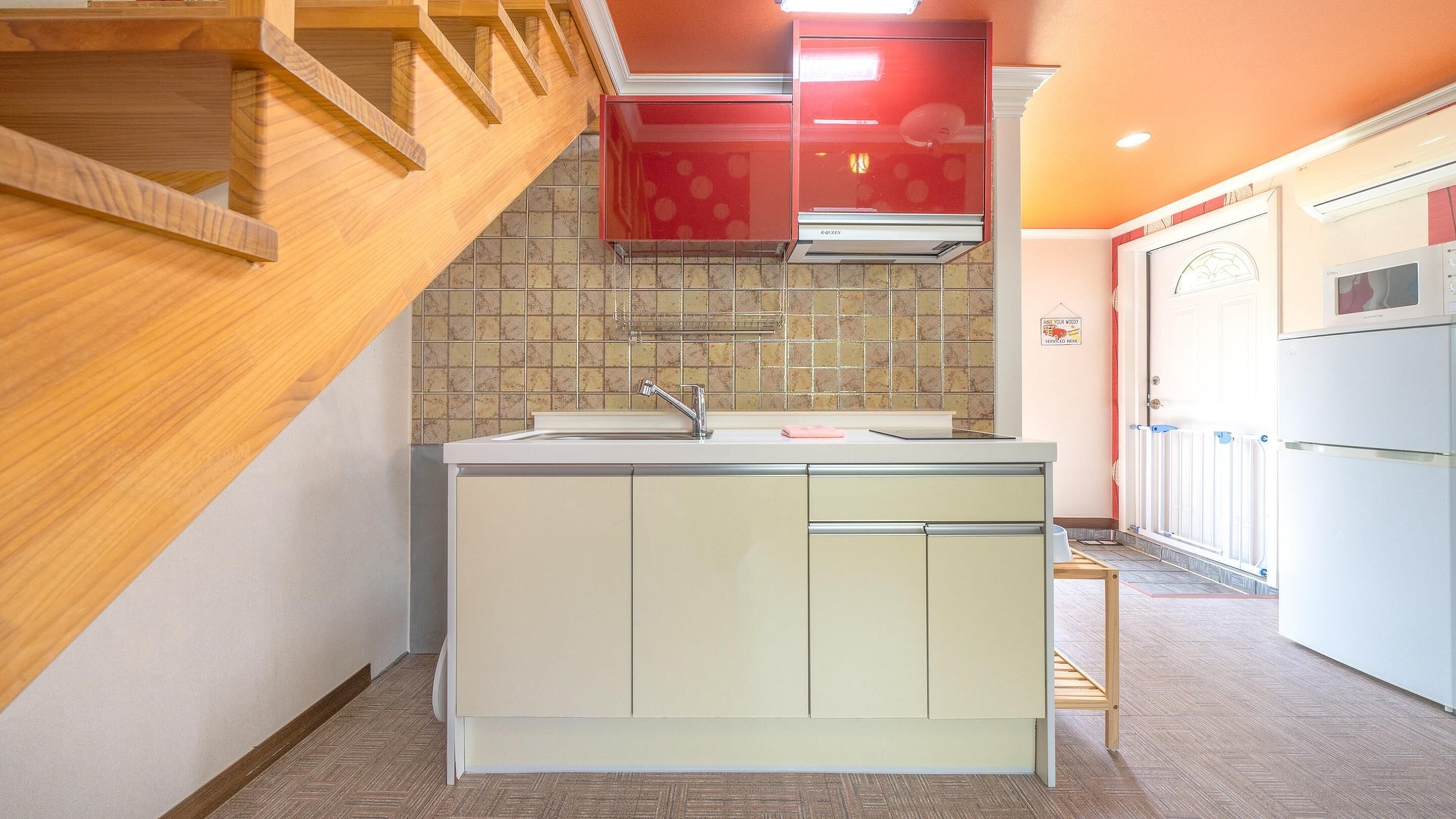 A compact kitchen with a wooden staircase, a tiled backsplash, and a built-in refrigerator.