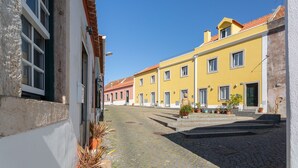 A cobblestone street lined with yellow buildings, some with balconies and potted plants. - Palace Guest Inn (Queluz)