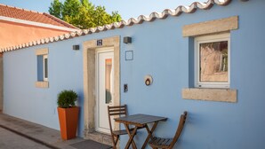A blue building with a tiled roof, a door with a number plate, a window, and a small table with chairs. - Palace Guest Inn (Queluz)