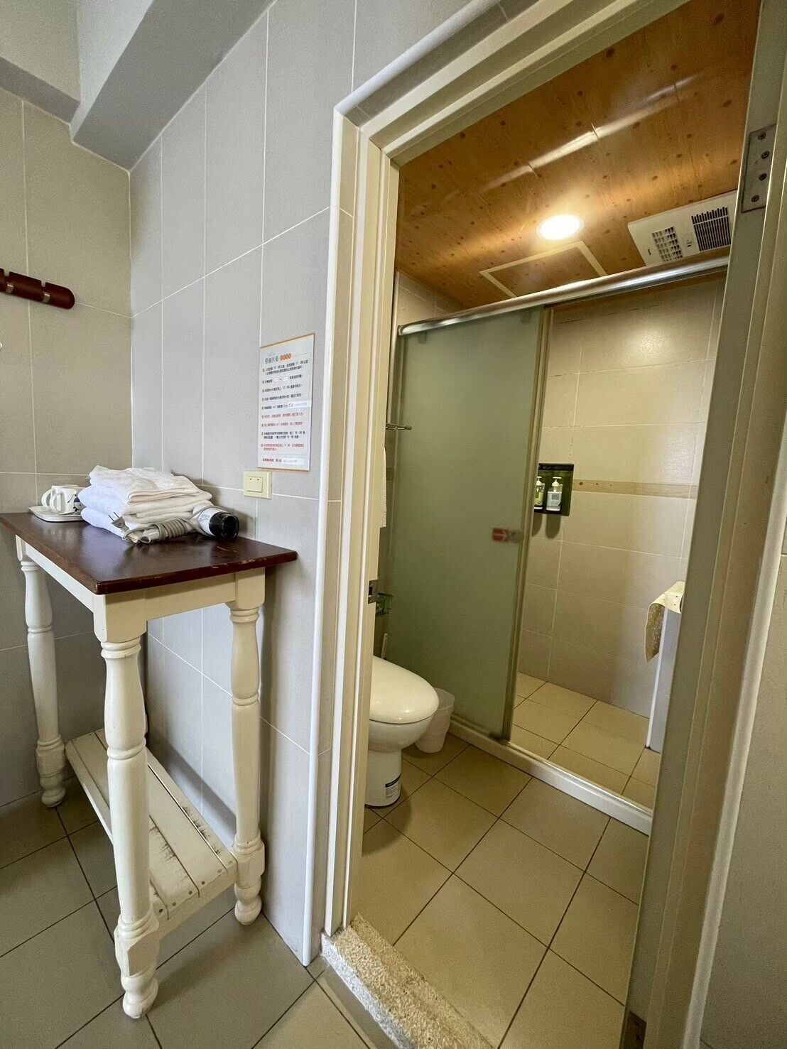 A bathroom with a toilet, a shower, and a small table with towels.