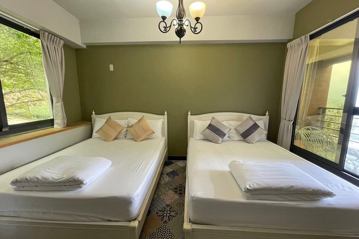 A room with two single beds, a chandelier, and large windows with curtains.