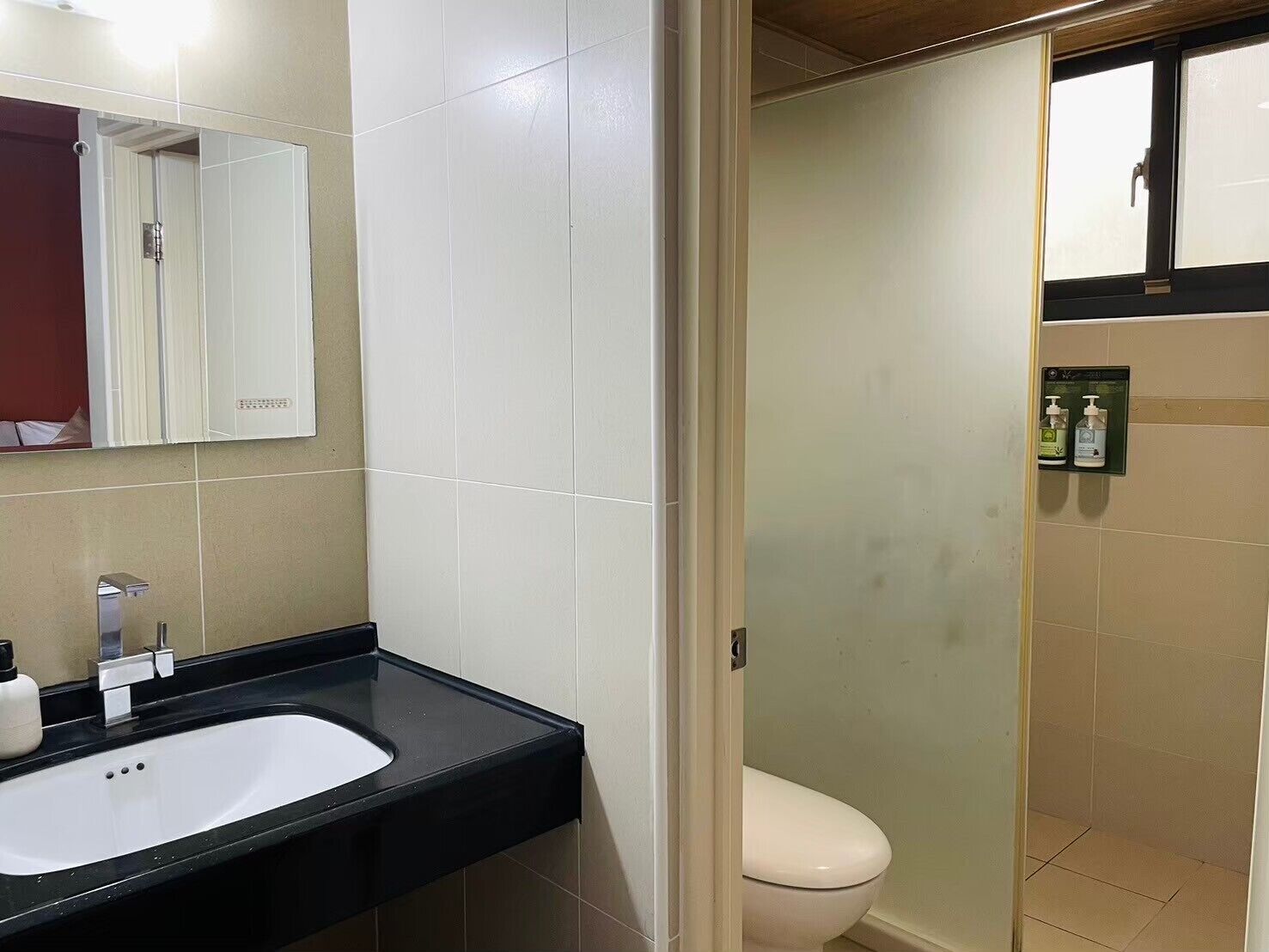 A bathroom with a white sink, mirror, and toilet. There is a shower area visible through the door.