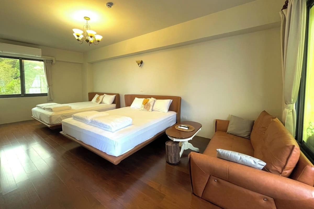 A hotel room with two single beds, a sofa, a small table, and a large window.