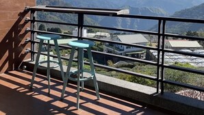 Un balcon donnant sur des montagnes lointaines, un petit tabouret et une rambarde.