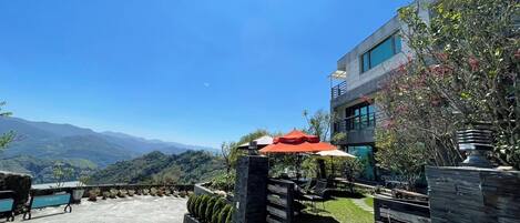 Terraza en la azotea con mobiliario exterior, vistas a montañas lejanas y un edificio moderno con amplios ventanales.