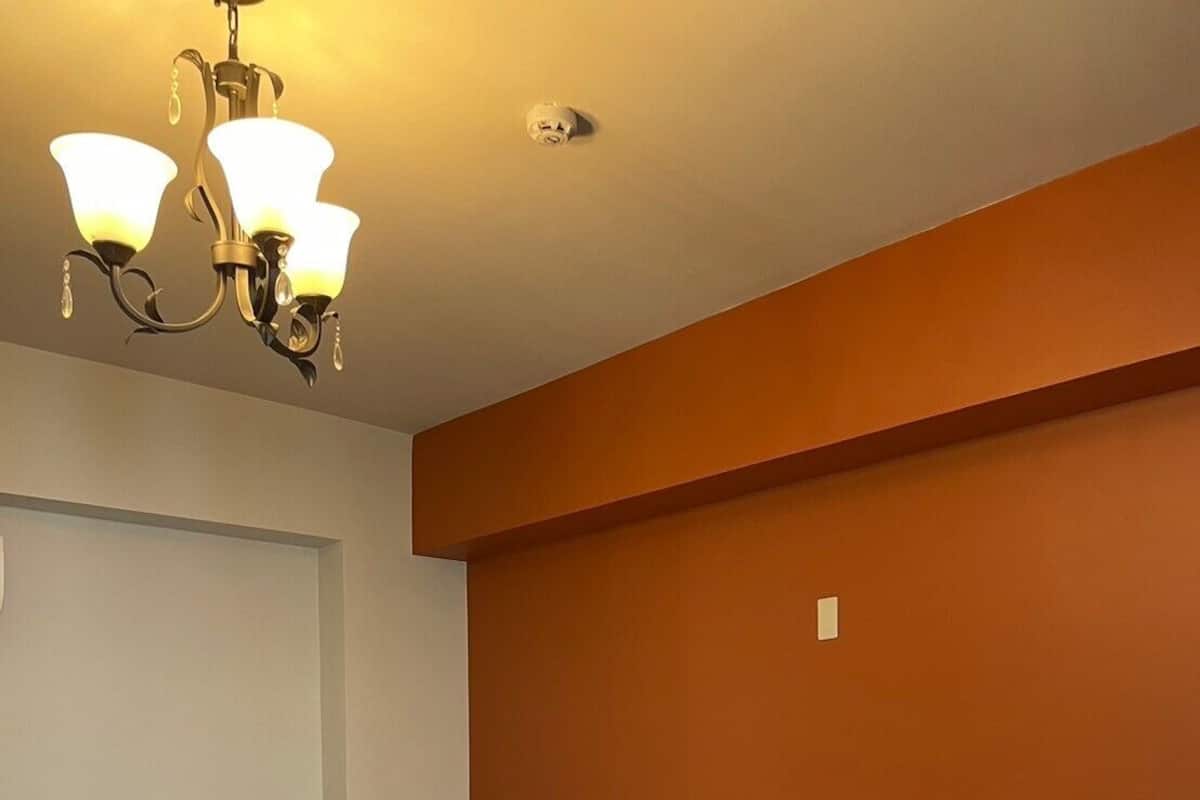 A neatly made bed with white linens and two decorative pillows, a wooden side table, and a wall-mounted light fixture.