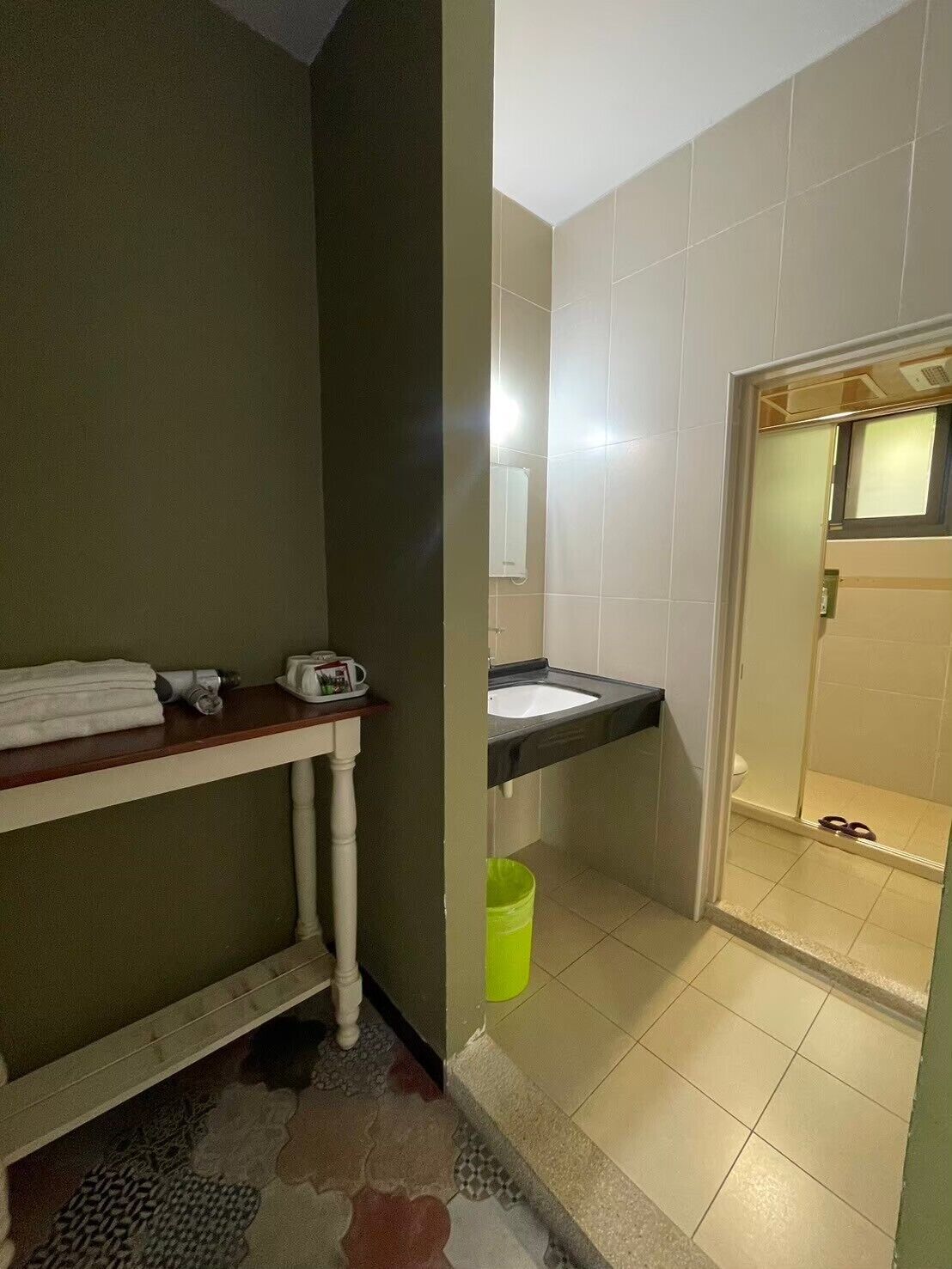 A bathroom with a sink, toilet, and shower area. There is a towel rack and a green trash bin.