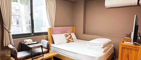 Habitación de hotel con cama, escritorio, silla, aire acondicionado y ventana con cortinas.